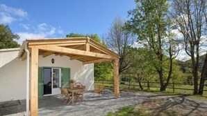 Une petite maison avec une pergola en bois, une table entourée de chaises et une terrasse en gravier.