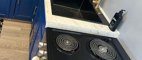 A kitchen with a black stove, blue cabinets, and a marble countertop.