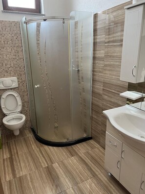 A modern bathroom with a glass shower enclosure, a toilet, and a sink with cabinets. - Peja INN (Pec)