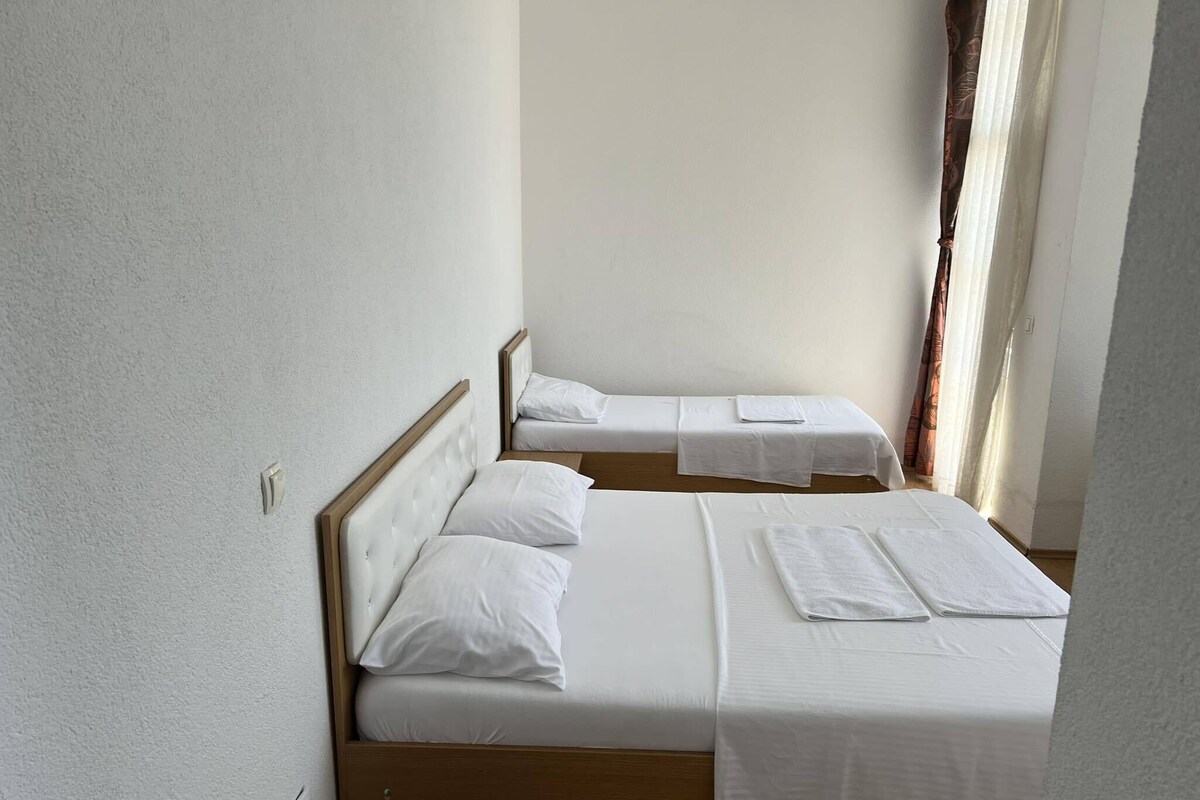 A room with two single beds, each with white linens and pillows, a wooden headboard, and a small wooden table.