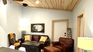 Un salon chaleureux avec un canapé en cuir marron, une table basse en bois, un tapis à motifs et une lampe verte.