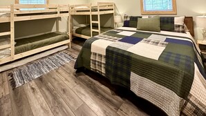 Une chambre avec des lits superposés, un grand lit, un ventilateur de plafond et une fenêtre avec des stores.