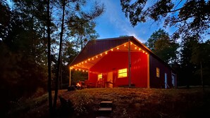 Une cabane en bois rouge, dotée d’un porche, entourée d’arbres, et où brûle un feu à l’intérieur.