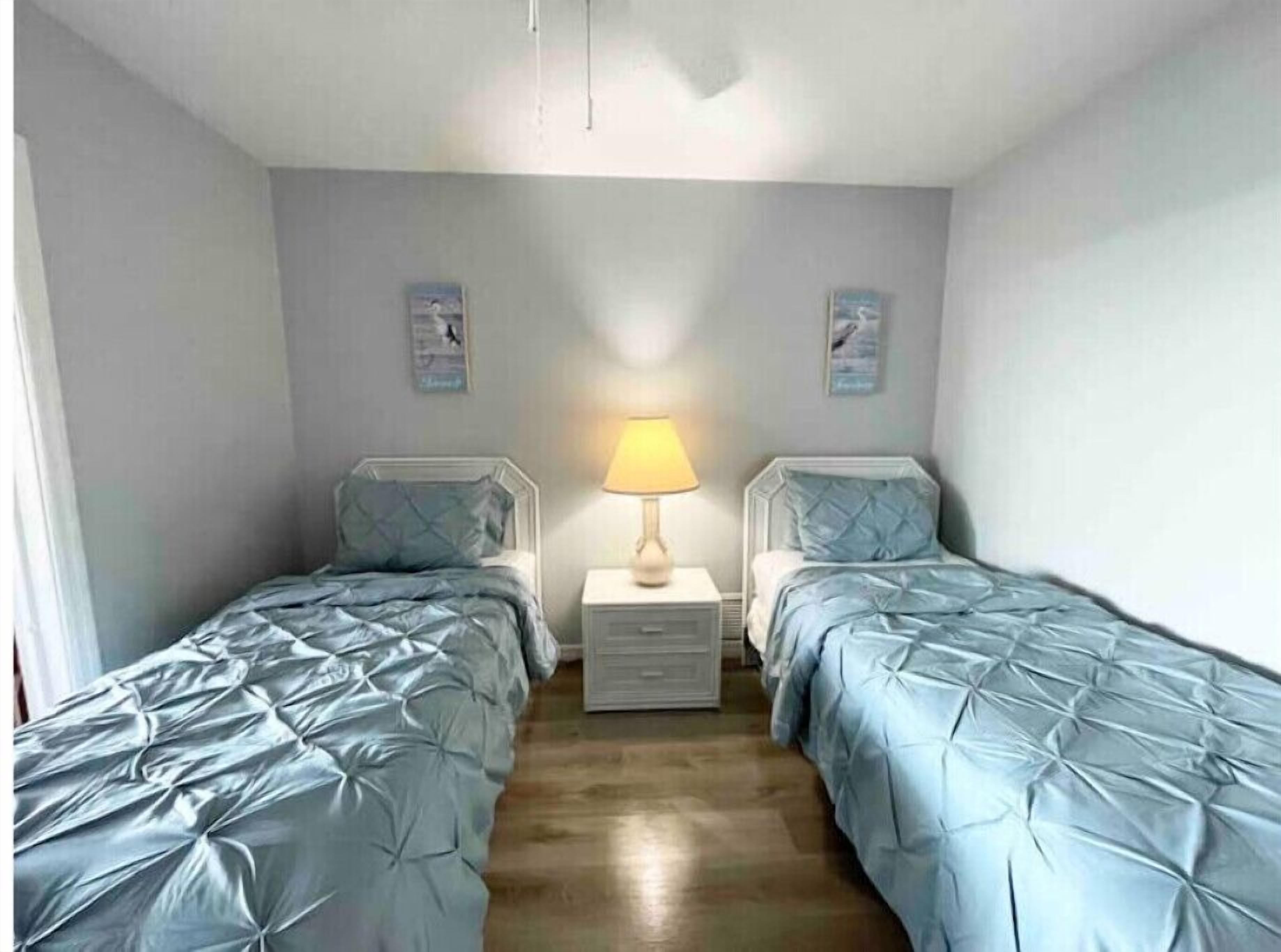 A room with two single beds, a bedside table with a lamp, and a small drawer unit.