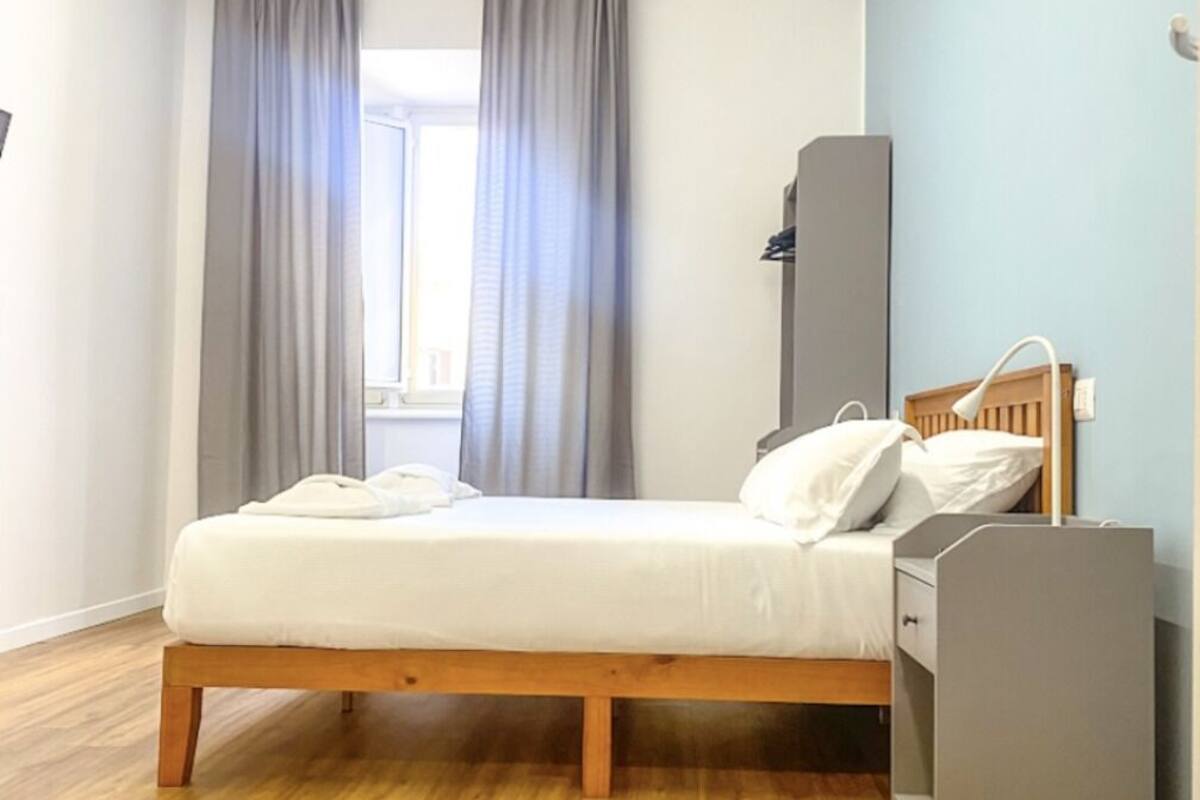 A bedroom with a wooden bed, grey curtains, a grey wardrobe, and a wooden floor.