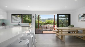 Una cocina moderna con armarios blancos, una mesa de comedor de madera y vistas a un jardín exuberante a través de amplios ventanales.
