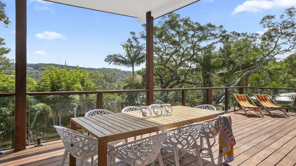 Una terraza de madera con una mesa y sillas, con vistas a un paisaje exuberante de árboles y colinas.