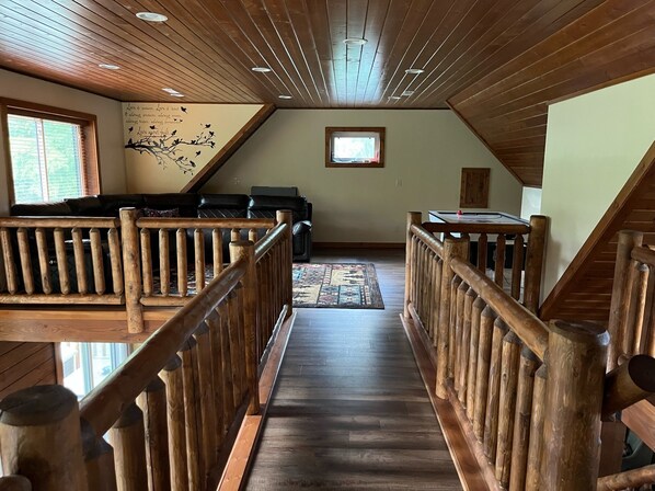 A wooden interior with a central staircase, a ceiling with recessed lighting, and a window with a view. - Charming 3,800 sq feet log house in Waupaca County. (Ogdensburg)
