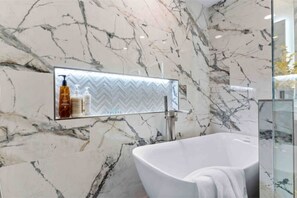 Un baño con bañera independiente, paredes de mármol y cabina de ducha de vidrio.