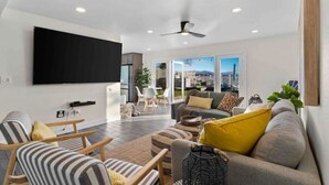 A modern living room with a flat-screen TV, a ceiling fan, and a large window offering a city view. - Upscale Resort House /Views, Saltwater Pool/Spa !
 (Spring Valley)
