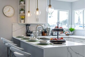 Una cocina moderna con una isla de mármol, luces colgantes, un reloj y una ventana con vistas.