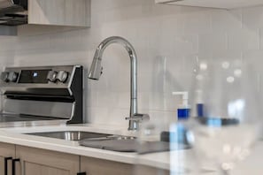 Une cuisine moderne dotée d’une hotte en acier inoxydable, d’un robinet élégant et d’un plan de travail blanc.