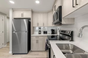 Una cocina moderna con electrodomésticos de acero inoxidable, armarios de madera clara y encimera blanca.