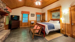 Una habitación acogedora con cama, paredes de madera, ventilador de techo, televisor y chimenea de piedra.