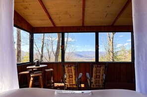 Cabaña con vistas a montañas a través de amplios ventanales. Un cartel indica disponibilidad de abril a octubre.