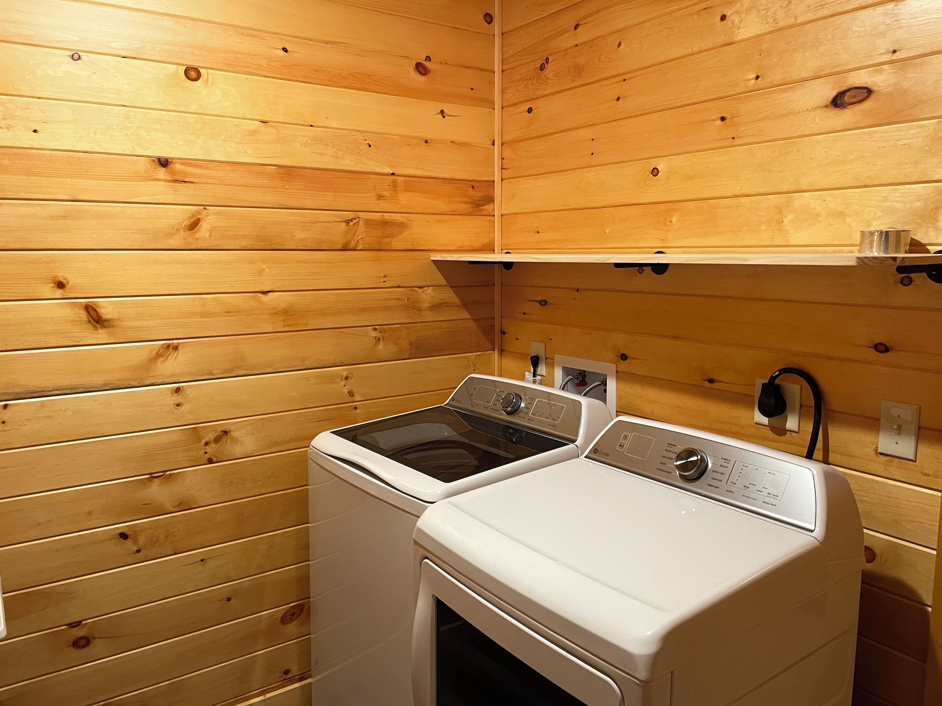 A laundry room with wooden walls and two washing machines.