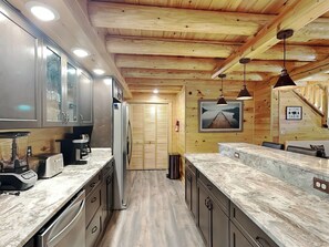 A modern kitchen with wooden ceiling beams, granite countertops, and stainless steel appliances.