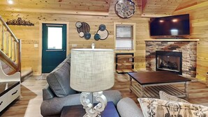 Ein gemütliches Wohnzimmer mit einer Couch, einer Lampe, einem Kamin, einem Fernseher und einer Wanduhr.