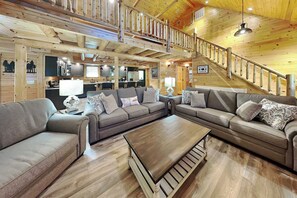 A cabin interior with a living area, kitchen, and a staircase leading to an upper level. - Alpine Valley by Taylor Made Deep Creek (McHenry)