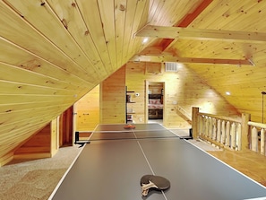 A ping pong table in a wooden room with a sloped ceiling and a small staircase.