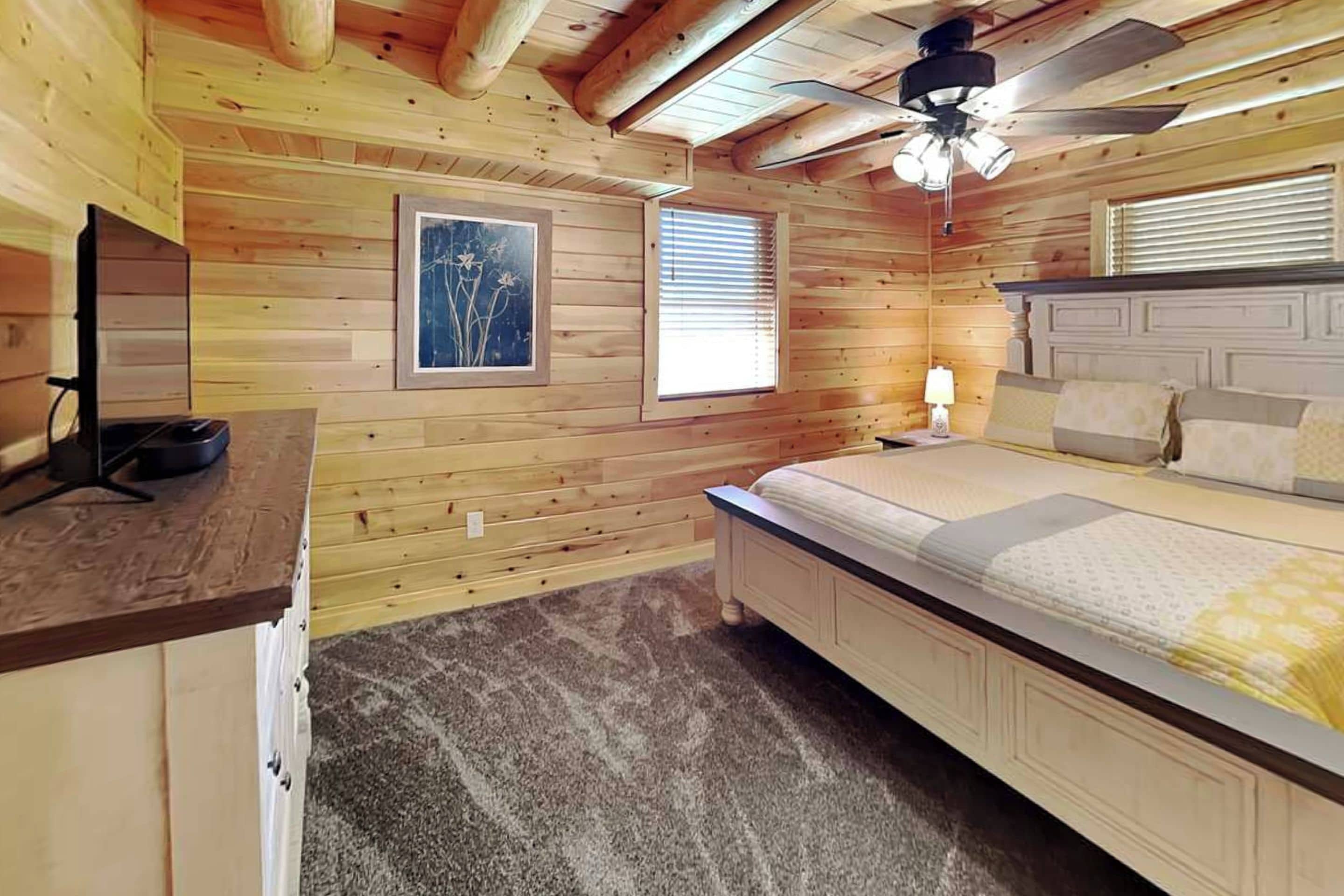 Une chambre avec des murs en bois, un lit, un bureau et un ventilateur de plafond.