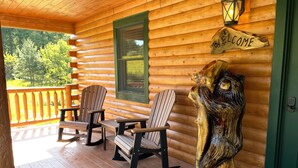 Eine Holzhütte mit Veranda, ausgestattet mit Adirondack-Stühlen und einem Willkommensschild.