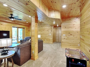 A cozy cabin interior with a sofa, a small table, a ceiling fan, and a foosball table.