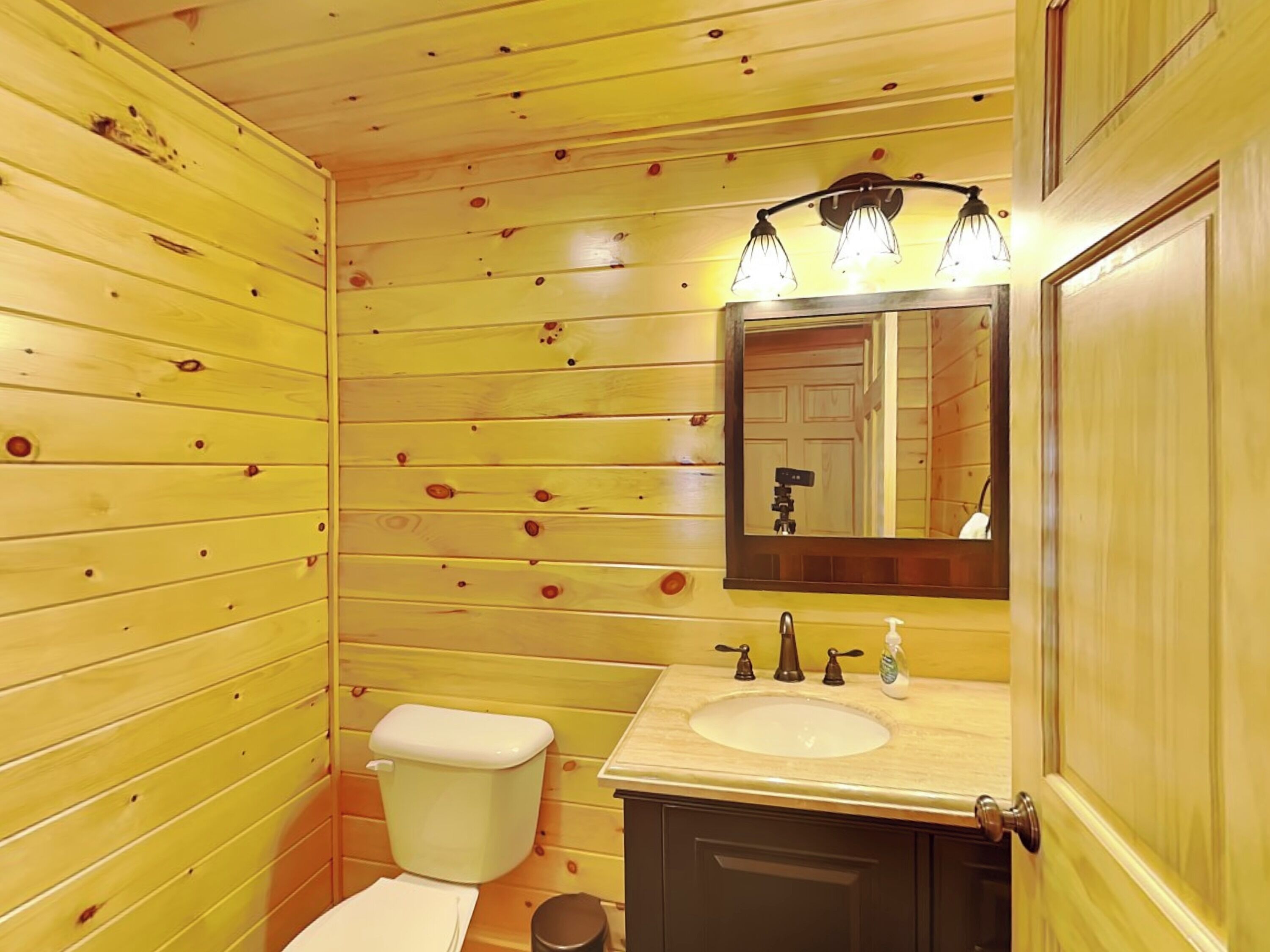 A wooden-paneled bathroom with a toilet, sink, and mirror.