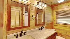 Casa de banho de cabana de madeira com duas pias, sanita e um espelho grande com luzes acima.