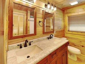 A wooden cabin bathroom with two sinks, a toilet, and a large mirror with lights above.