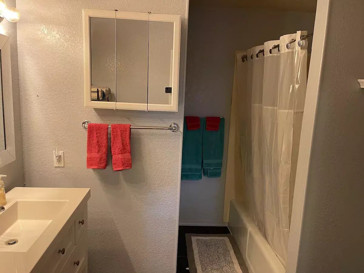 Casa de banho com lavatório branco, espelho e porta-toalhas. Toalhas vermelhas e azul-petróleo penduradas no porta-toalhas.