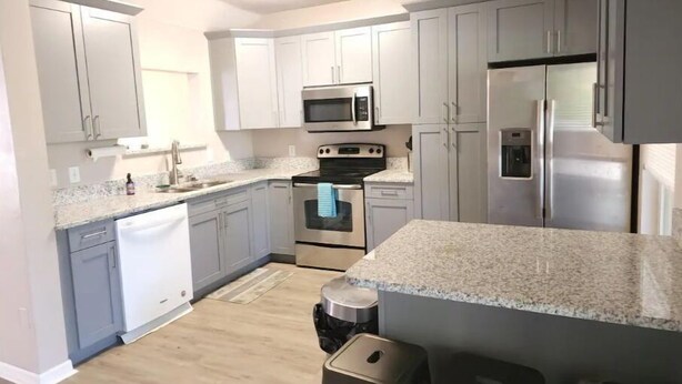A modern kitchen with grey cabinets, stainless steel appliances, and a granite countertop.