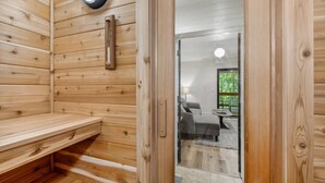 A wooden sauna room with a bench and a door leading to a living area with a sofa and a table. - Sandhill - Luxury Cabin (Flathead County)