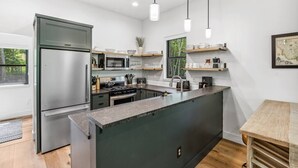 A modern kitchen with a central island, stainless steel appliances, and wooden shelves. - Sandhill - Luxury Cabin (Flathead County)