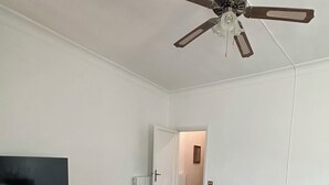 Ein Zimmer mit Deckenventilator, einem Bett, einem Schreibtisch mit Stuhl und einem Fernseher.