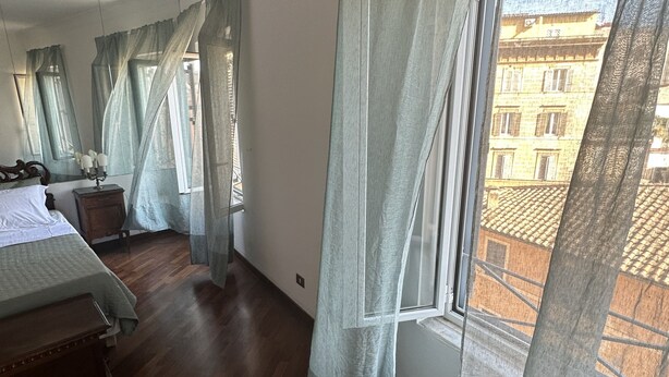 Ein Schlafzimmer mit Holzboden, einem Bett, einem Nachttisch und einem Fenster mit leichtem Vorhang.