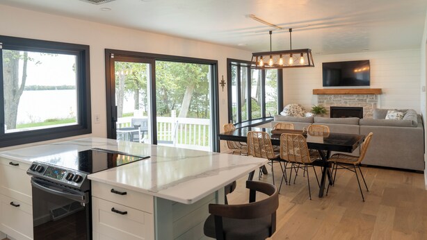 Una cocina moderna con una isla, comedor con sillas de mimbre, un sofá gris y una chimenea.