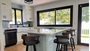 Cocina moderna con una isla grande, taburetes de bar y vistas a árboles a través de amplias ventanas.