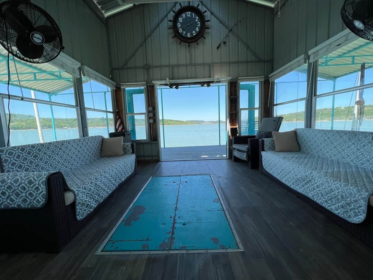 A room with two patterned sofas facing a large window, a clock on the wall, and a fan on the ceiling.