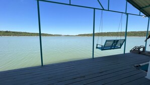 Une terrasse en bois avec un fauteuil suspendu, donnant sur une étendue d’eau calme et une côte lointaine.