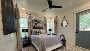 Une chambre à coucher comprenant un lit, un ventilateur de plafond, une fenêtre, une porte et un miroir fixé au mur.