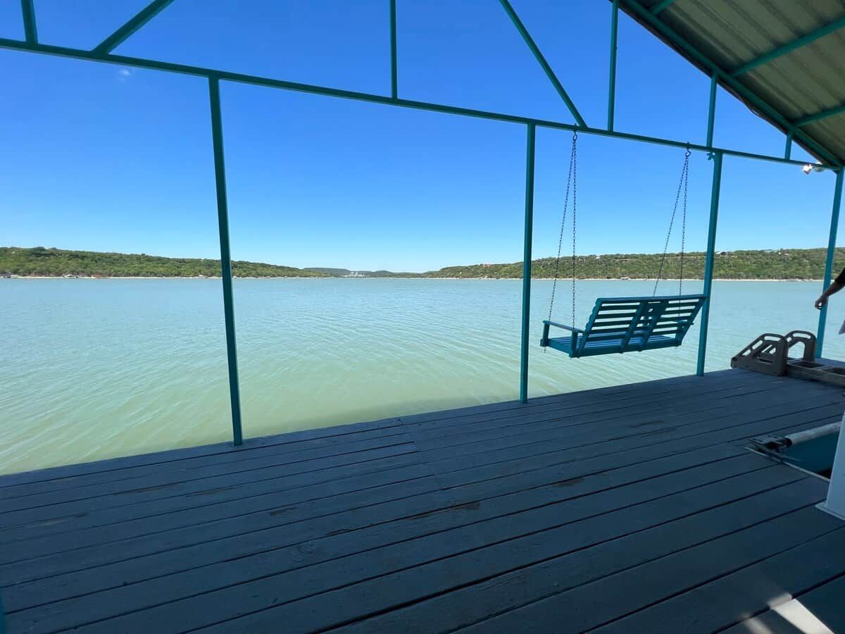 A wooden deck with a swing chair overlooking a calm body of water.
