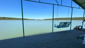 A wooden deck with a swing chair overlooking a calm body of water.