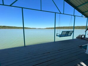 Une terrasse en bois avec un fauteuil suspendu donnant sur une étendue d’eau calme.