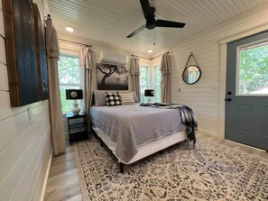 Une chambre à coucher avec un lit, un ventilateur de plafond, une fenêtre et une porte.