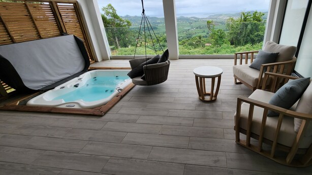 En balkon med jacuzzi, træmøbler og udsigt over et grønt landskab.