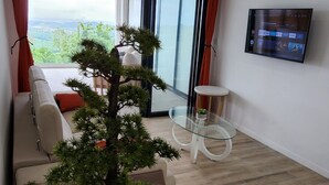 En moderne stue med et stort bonsai-træ i potte, et sofabord i glas, en sofa og et fjernsyn ophængt på væggen.