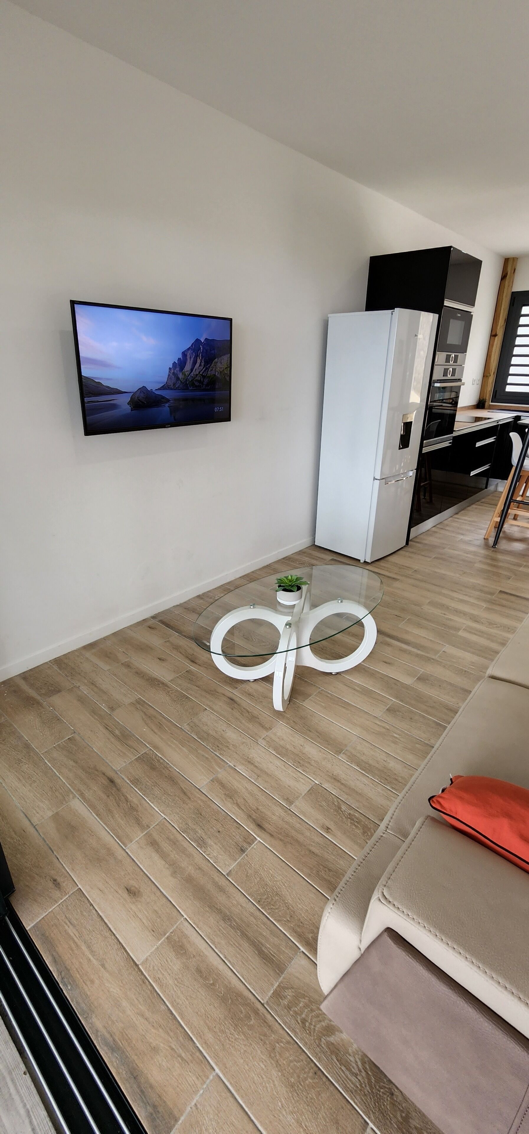 Een moderne keuken met een flatscreen televisie, een witte koelkast en een glazen salontafel met een klein plantje.