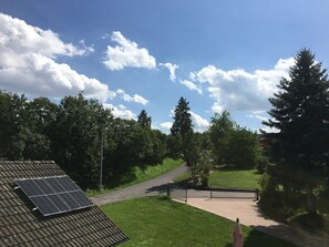 A rooftop with solar panels, a paved path, and a gate leading to a green area with trees.