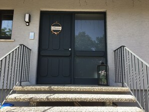 A black door with a welcome sign, a small window, and a flower lantern on the steps.